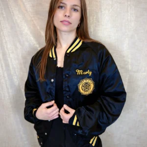 Model wearing a vintage black bomber jacket with striped yellow collar, cuffs, and waistband, and the word "Marty" embroidered in yellow on the left chest.