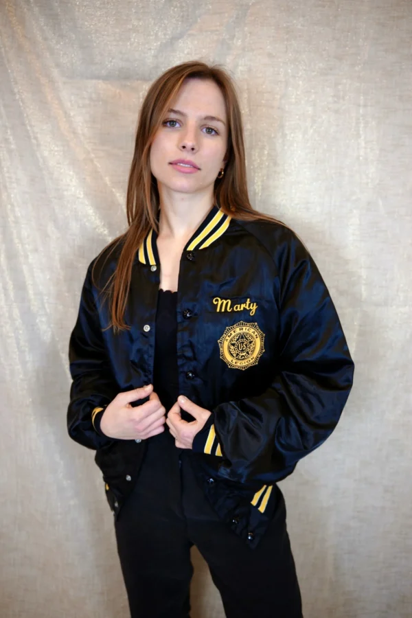 Model wearing a vintage black bomber jacket with striped yellow collar, cuffs, and waistband, and the word "Marty" embroidered in yellow on the left chest.