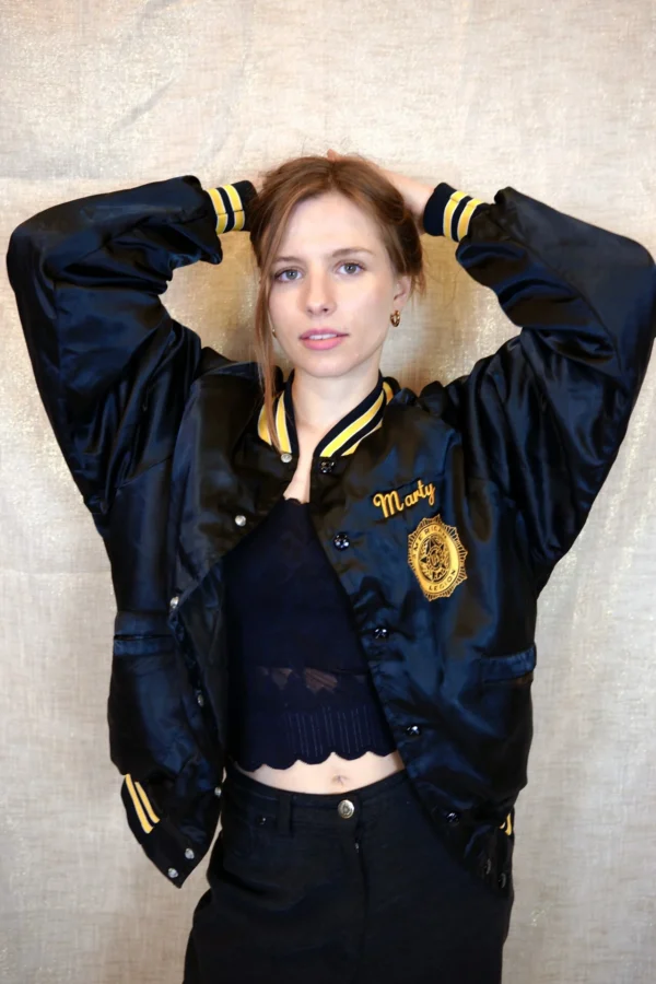 Model wearing a vintage black bomber jacket with snap closure and yellow stripe detail.