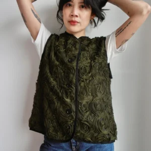 Model wearing a khaki green vest with mesh floral pattern, black trim and buttons, made sustainably from deadstock polyester fabric.