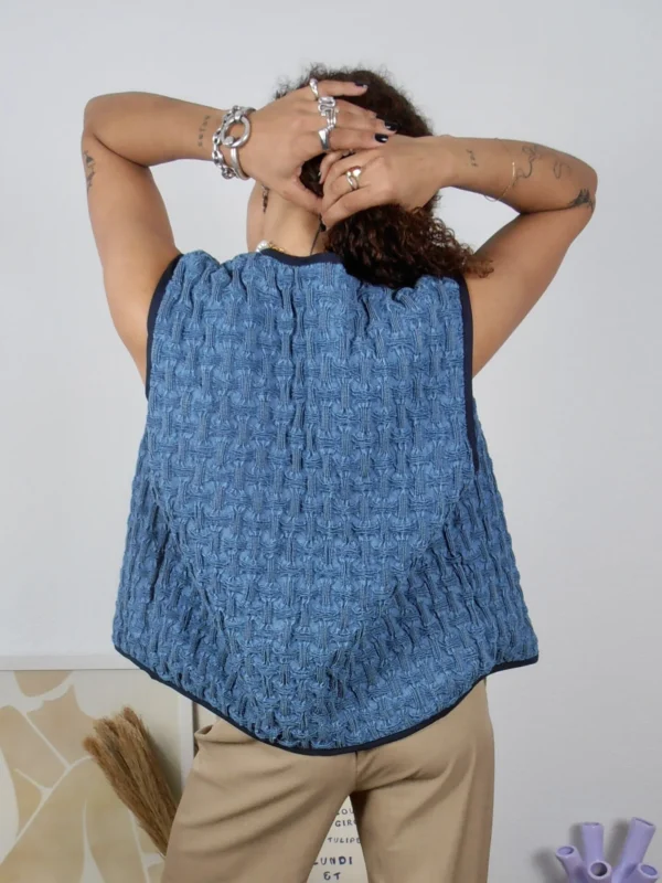 Backside of a textured denim vest with black buttons and navy trim, made from 100% ethically sourced cotton.