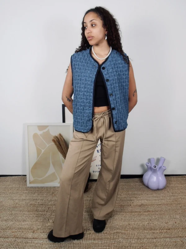 Model wearing a textured denim vest with black buttons and navy trim, made from ethically sourced cotton, layered over a black tank top.