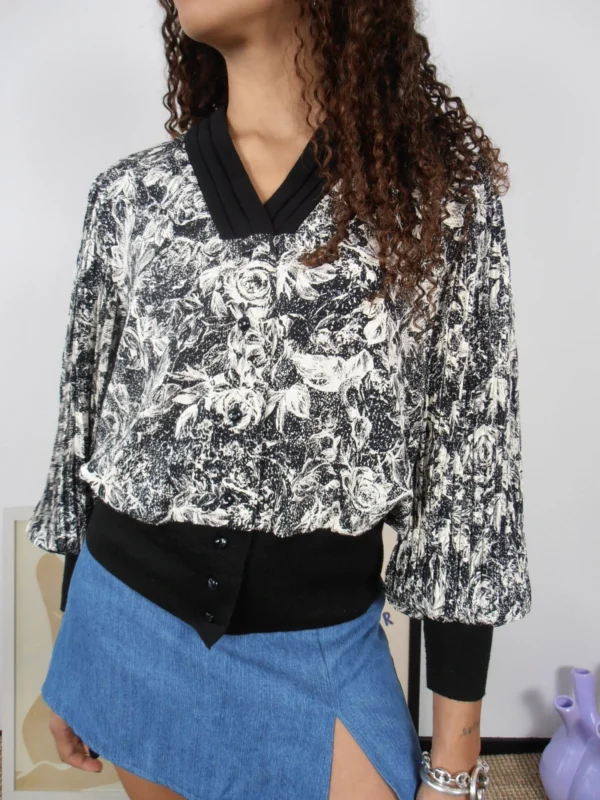 Close-up of a vintage black and white floral blouse with black collar, cuffs and waistband.