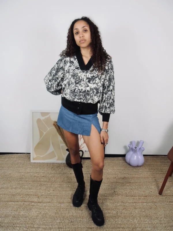 Model wearing a vintage black and white floral blouse, denim skort, and black boots.
